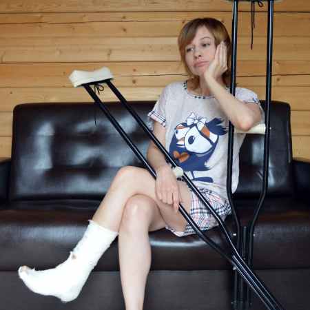 young sad woman with broken leg on sofa